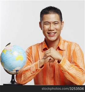 Portrait of a mid adult man smiling and sitting besides a desktop globe