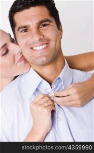 Portrait of a mid adult man smiling with a young woman kissing him from behind