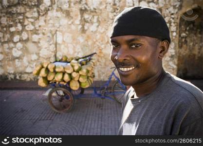 Portrait of a mid adult man smiling with coconuts on a rickshaw in the background, Santo Domingo, Dominican Republic