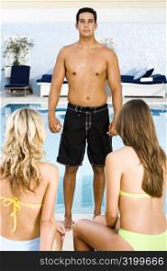 Portrait of a mid adult man standing in front of two young women at the poolside