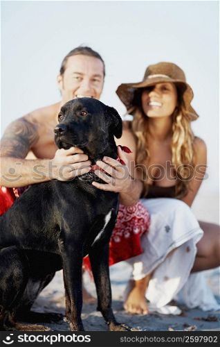 Portrait of a mid adult man stroking a dog with a young woman beside him on the beach