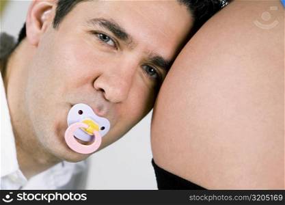 Portrait of a mid adult man sucking a pacifier and listening to a pregnant woman&acute;s abdomen