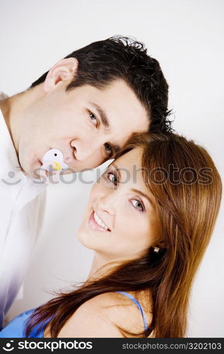 Portrait of a mid adult man sucking a pacifier with a young woman smiling