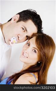Portrait of a mid adult man sucking a pacifier with a young woman smiling