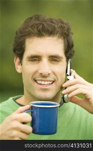 Portrait of a mid adult man talking on a mobile phone holding a cup of coffee