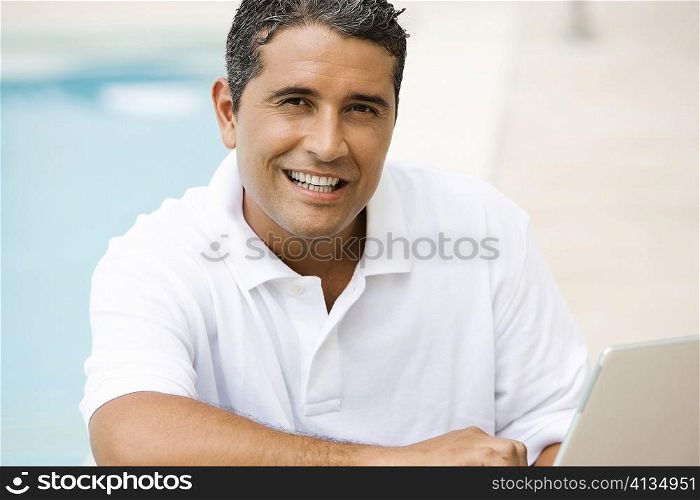 Portrait of a mid adult man using a laptop at the poolside