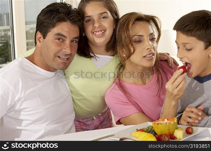 Portrait of a mid adult man with his daughter and mid adult woman feeding her son a strawberry
