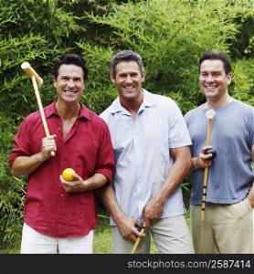 Portrait of a mid adult man with two mature men holding croquet mallets and balls