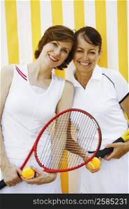 Portrait of a mid adult woman and a mature woman holding tennis rackets and tennis balls