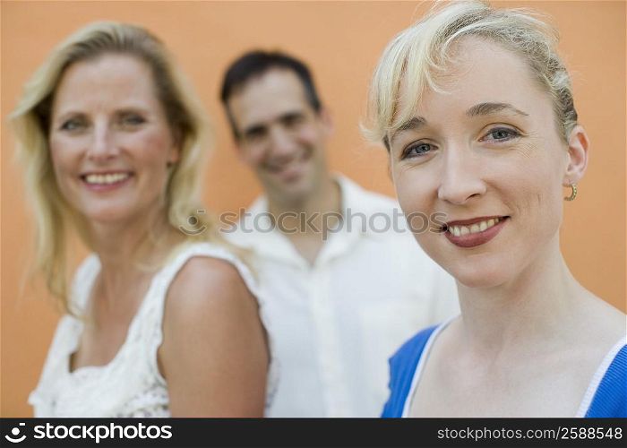 Portrait of a mid adult woman and a mature woman with a mid adult man smiling in the background