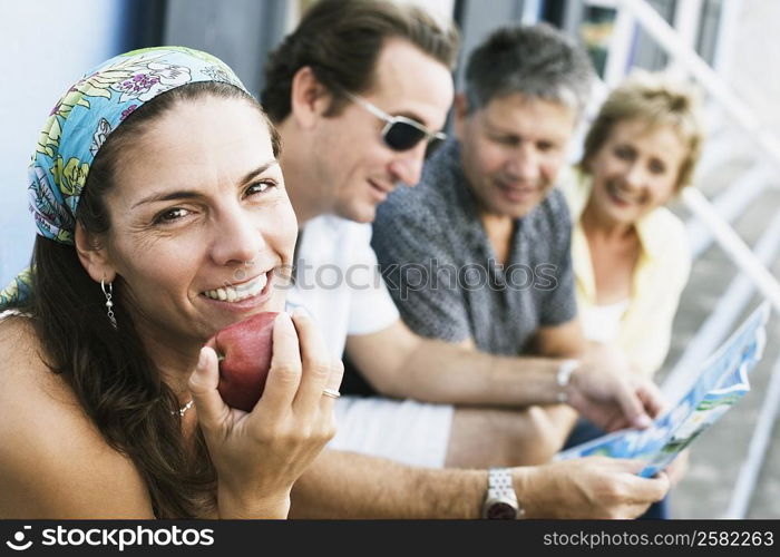 Portrait of a mid adult woman eating an apple with her friends sitting beside her