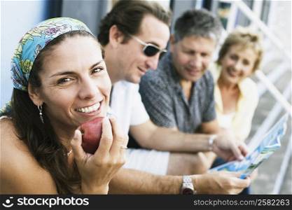 Portrait of a mid adult woman eating an apple with her friends sitting beside her