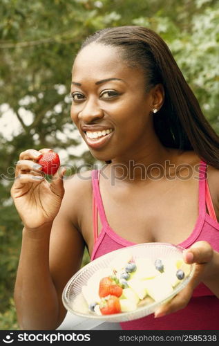 Portrait of a mid adult woman holding a bowl of fruit salad and smiling