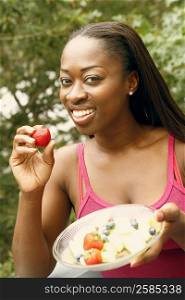 Portrait of a mid adult woman holding a bowl of fruit salad and smiling