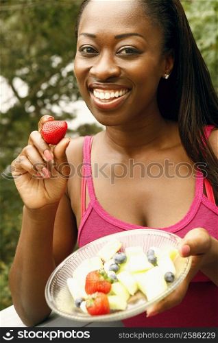 Portrait of a mid adult woman holding a bowl of fruit salad and smiling