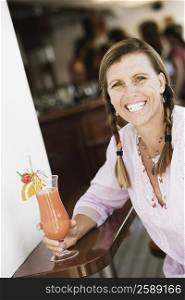Portrait of a mid adult woman holding a glass of cocktail and smiling