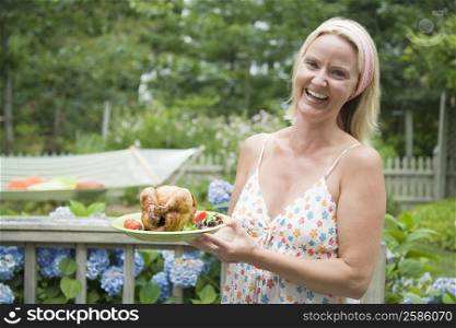 Portrait of a mid adult woman holding a plate of roast chicken and smiling
