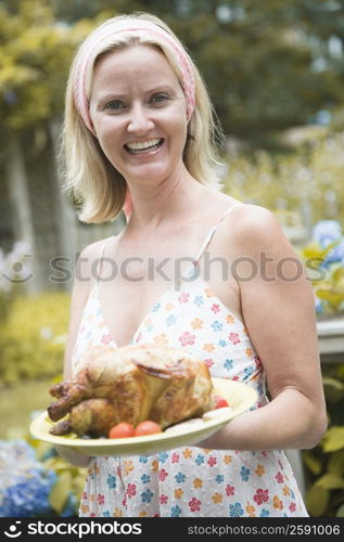 Portrait of a mid adult woman holding a plate of roast chicken and smiling