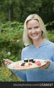 Portrait of a mid adult woman holding a plate of sushi and smiling