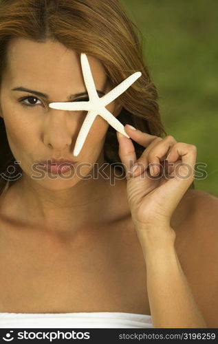 Portrait of a mid adult woman holding a star fish in front of her eye