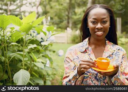 Portrait of a mid adult woman holding a tea cup with a saucer in a park