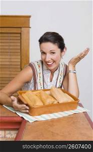 Portrait of a mid adult woman laughing with a tray of breads in the kitchen