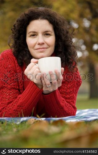 Portrait of a mid adult woman lying in a park and holding a coffee cup