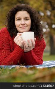 Portrait of a mid adult woman lying in a park and holding a coffee cup