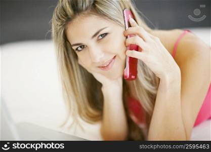 Portrait of a mid adult woman lying in front of a laptop and talking on a mobile phone