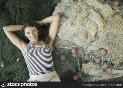 Portrait of a mid adult woman lying on commercial fishing nets and smiling