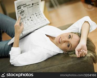 Portrait of a mid adult woman lying on the bed and holding a newspaper