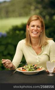 Portrait of a mid adult woman sitting at a table with a plate of vegetable salad in front of her