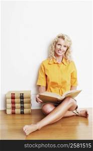 Portrait of a mid adult woman sitting cross-legged on the floor with a book and smiling