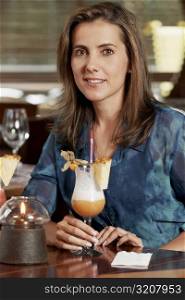 Portrait of a mid adult woman sitting in a restaurant and holding a glass of pina colada