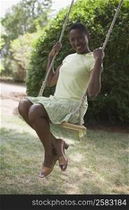 Portrait of a mid adult woman sitting on a rope swing and smiling