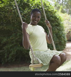 Portrait of a mid adult woman sitting on a rope swing and smiling