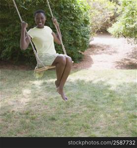 Portrait of a mid adult woman sitting on a rope swing and smiling