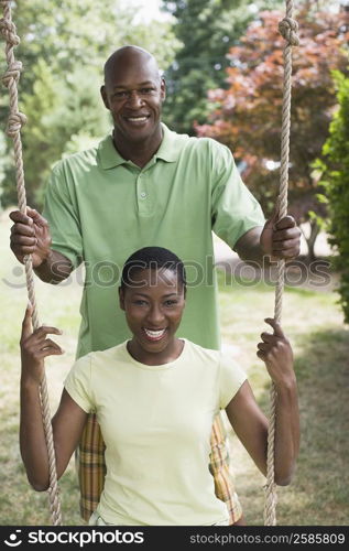 Portrait of a mid adult woman sitting on a rope swing with a mature man pushing her