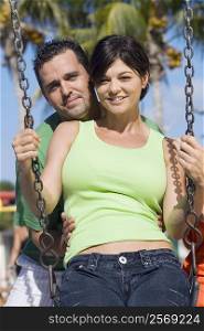 Portrait of a mid adult woman swinging on a swing with a mid adult man standing behind her and smiling