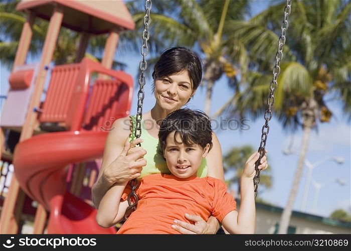 Portrait of a mid adult woman swinging on a swing with her son and smiling