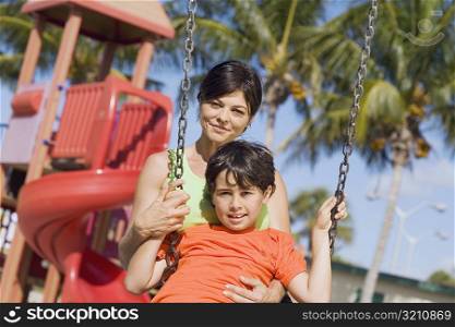 Portrait of a mid adult woman swinging on a swing with her son and smiling