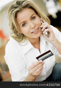 Portrait of a mid adult woman talking on a mobile phone and holding a credit card