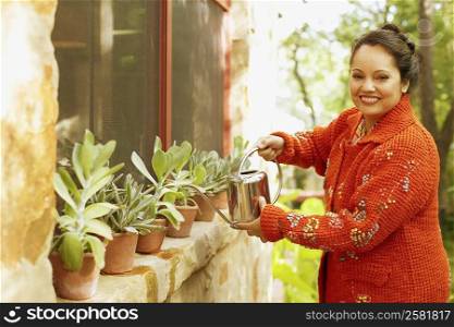 Portrait of a mid adult woman watering plants with a watering can and smiling