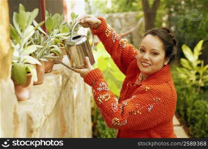 Portrait of a mid adult woman watering plants with a watering can and smiling