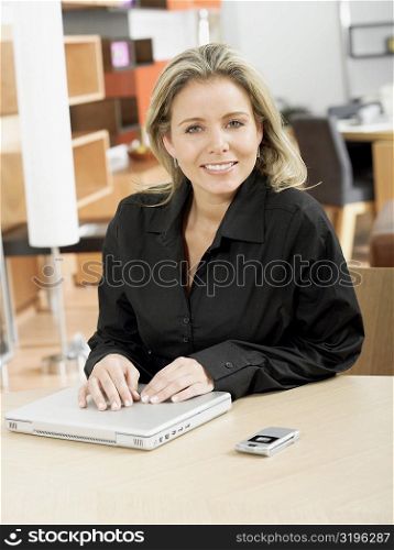 Portrait of a mid adult woman with her hands on a laptop and smiling