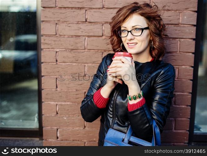 Portrait of a modern young woman with coffee cup in hands, urban background