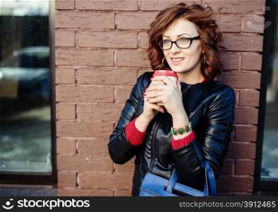 Portrait of a modern young woman with coffee cup in hands, urban background