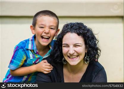 Portrait of a monther and her son outside on the lawn on a nice summer day, both looking at the camera and laughing happily. Son slightly behind mother with his hand on her sholder.
