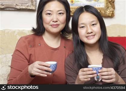Portrait of a mother and her daughter holding tea cups