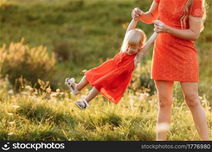 Portrait of a mother holds, throws up and spins the daughter on hands on nature on summer day vacation. Mom and girl playing in the park at the sunset time. Concept of friendly family. Close Up.. Portrait of a mother holds, throws up and spins the daughter on hands on nature on summer day vacation. Mom and girl playing in the park at the sunset time. Concept of friendly family. Close Up